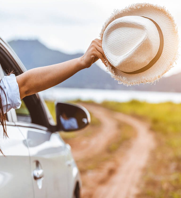 woman holding a hat out of an open car window